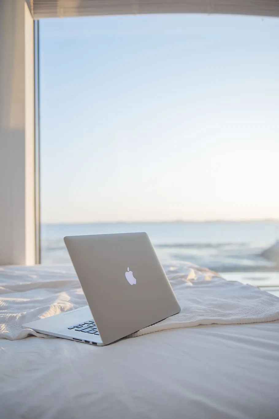 A laptop on a bed in front of a window looking out to sea
